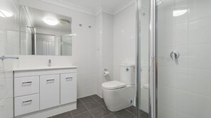 Une salle de bain moderne avec une douche à parois de verre, des toilettes blanches et un meuble-lavabo avec des tiroirs.