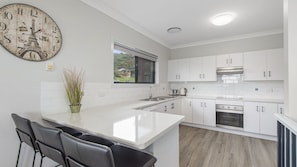 A modern kitchen with white cabinetry, a central island, a sink, and a stove. There is a large clock with the Eiffel Tower on the wall.
