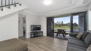 A modern living room with a flat-screen TV, a sofa, a wooden bench, and a patio area with a table and chairs.