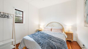 A bedroom with a bed, bedside tables, a window, and a wall-mounted drying rack. - The Tree House, 6 Gowing Street (Crescent Head)