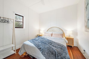 Une chambre à coucher avec un lit, des lampes de chevet, une fenêtre, un étendoir fixé au mur et un plancher en bois.
