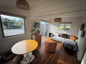 A room with a round wooden table, a sofa, a small ottoman, and a television on a cabinet. - THE TREE HOUSE - UNIQUE & PET FRIENDLY (Crescent Head)
