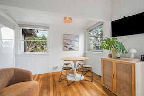 Une pièce avec une table ronde, trois tabourets, un meuble en bois, une grande plante et un tableau accroché au mur.
