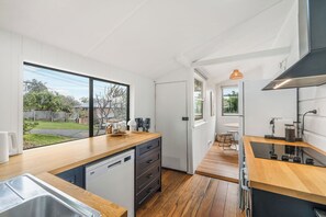Une cuisine moderne équipée d’un lave-vaisselle, de plans de travail en bois, d’une plaque de cuisson intégrée et offrant une vue sur le jardin arrière.
