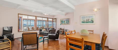 A spacious living area with a large window, a dining table, and a television.