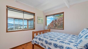 A bedroom with a bed, two windows, a fan, and a framed picture on the wall.