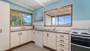 A kitchen with a dishwasher, stove, and a window with a view of greenery.