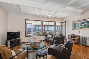 Una sala de estar con un ventanal grande, un televisor de pantalla plana, un sofá, una mesa de centro y una lámpara de pie.