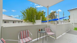 A covered outdoor area with two chairs and a table, surrounded by a white fence, under a clear sky.