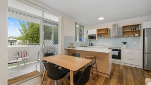 A modern kitchen with a dining area, featuring a large island, built-in appliances, and a view through the sliding glass door.