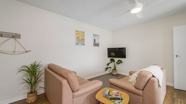 A living room with two sofas, a coffee table, a TV, and a ceiling fan.