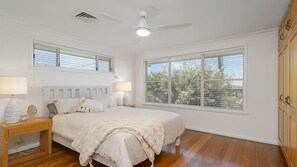 A bedroom with a bed, bedside lamps, a ceiling fan, and a large window with blinds.