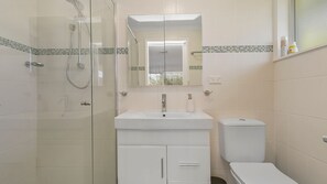 Un baño con ducha envuelta en vidrio, un lavabo blanco y un inodoro.