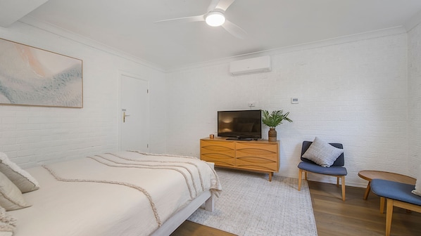 A bedroom with a bed, a TV on a wooden dresser, a chair, and a ceiling fan.
