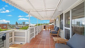 A covered outdoor balcony with a table and chairs, a sliding glass door, and a view of the surrounding area.