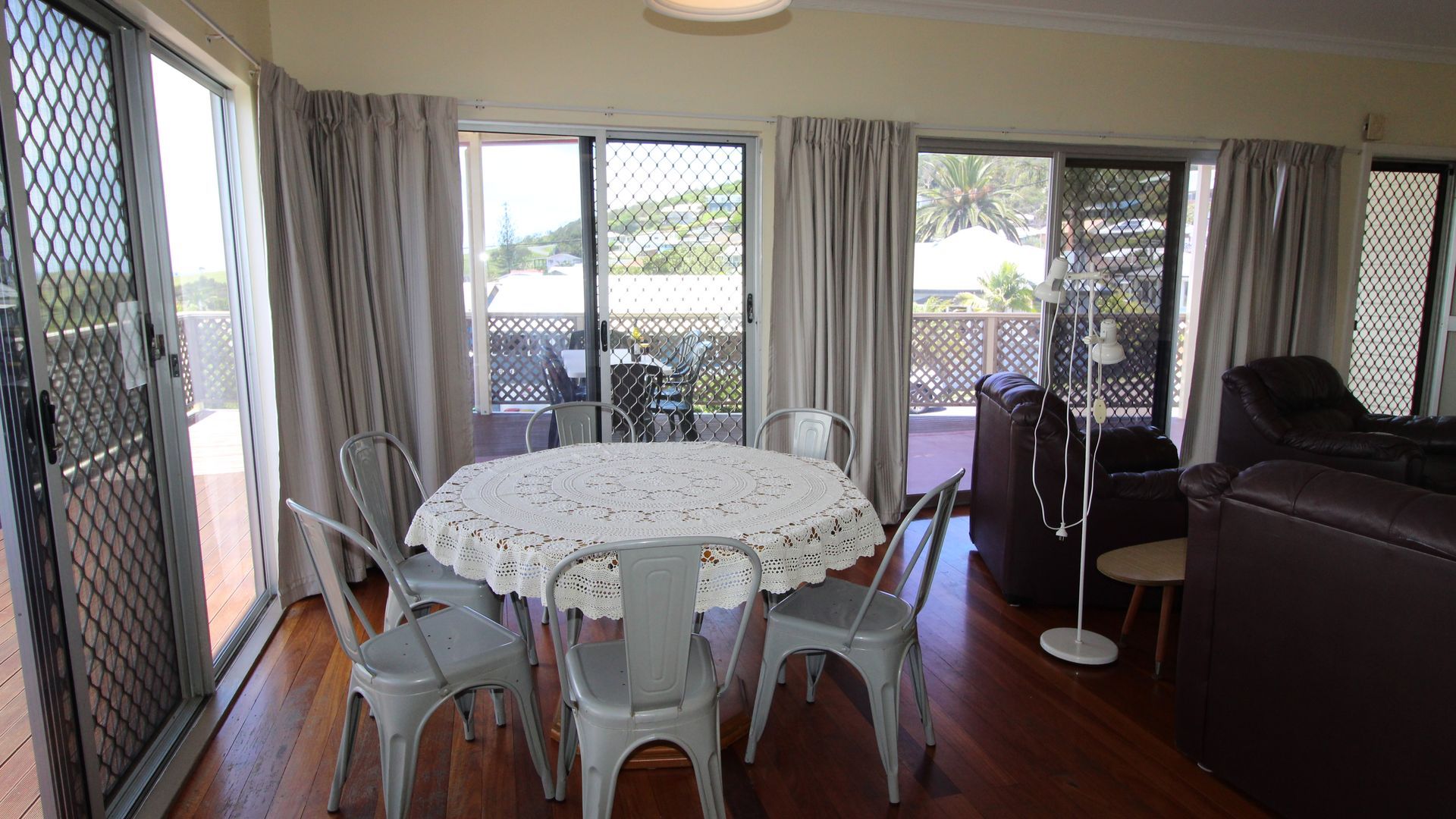 A room with a round table, chairs, a sofa, and a balcony with a view.