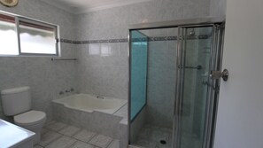 Un baño con inodoro, bañera y cabina de ducha con mampara de vidrio.