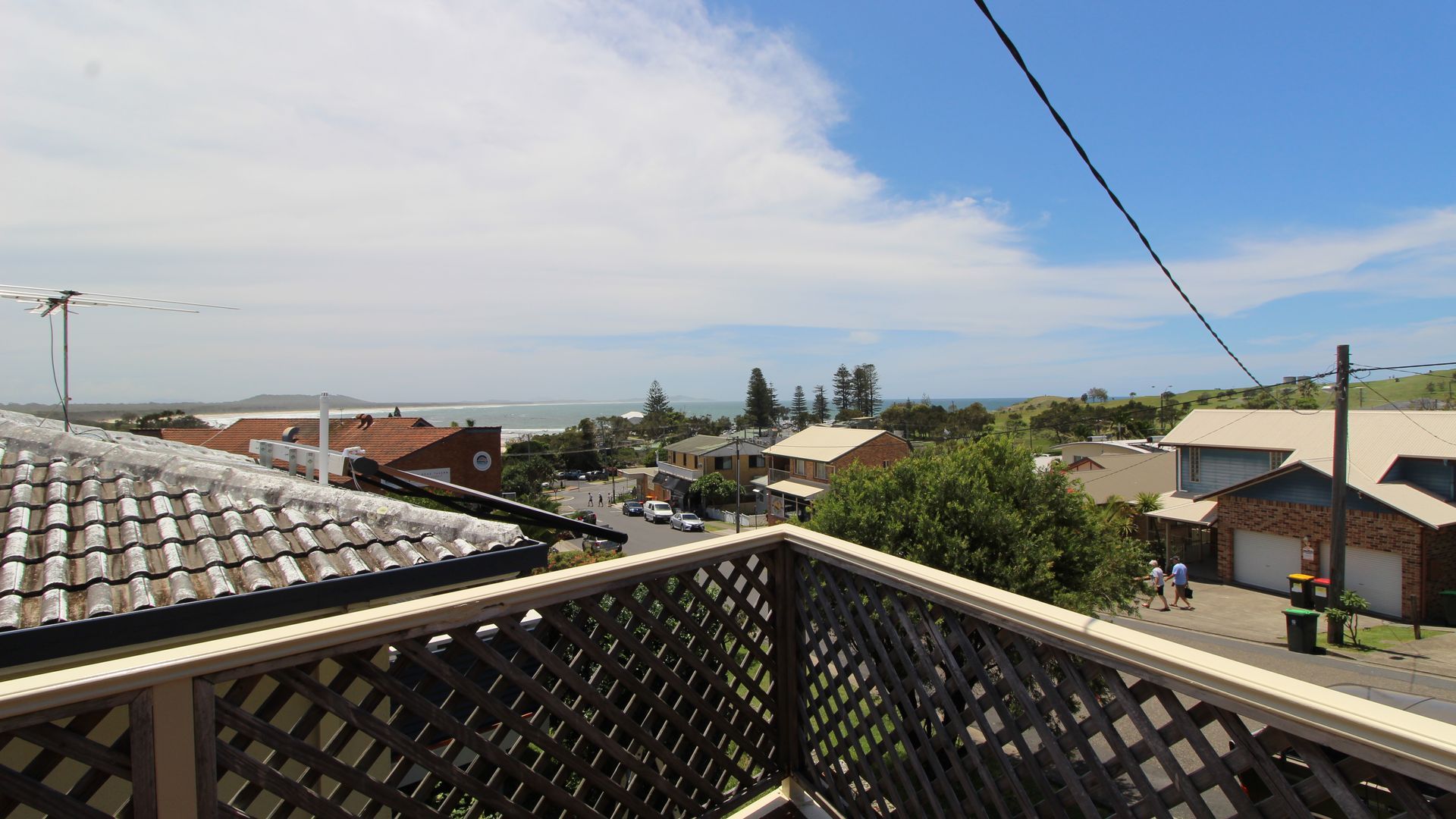 A residential area with a view of the ocean, houses with various roof styles, and a clear sky.
