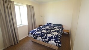 Un dormitorio con cama, cortinas, mesita de noche y lámpara.