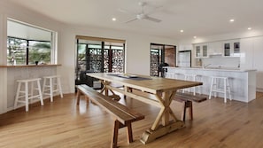A modern kitchen with a wooden dining table, white bar stools, and a built-in island.