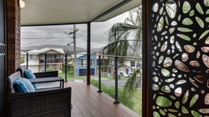 A covered outdoor seating area with wicker furniture and a view of residential buildings. - Seapoint Holiday House, 4 Gowing Street (Crescent Head)