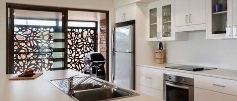 A modern kitchen with a stainless steel sink, a built-in oven, and white cabinetry.