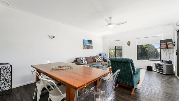 Ein modernes Wohnzimmer mit einem Holzes Esstisch, weißen Stühlen, einem grünen Sofa und einem Deckenventilator.