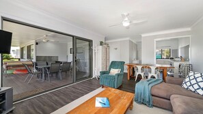 Una sala de estar moderna con un ventanal corredero que da a un patio exterior, un sofá, una mesa de centro y un comedor con mesa y sillas.