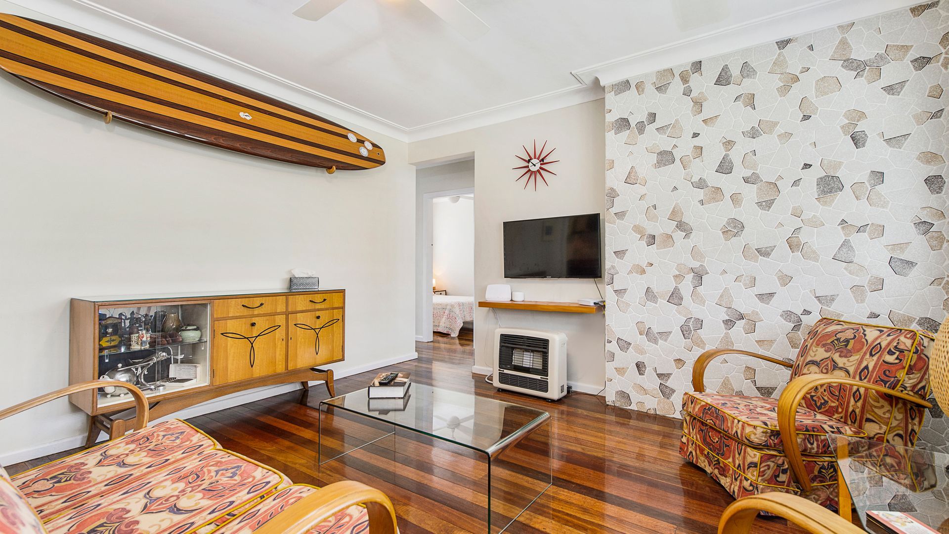 A living room with a glass coffee table, wooden furniture, a television, and a patterned wall.