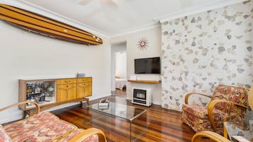 A living room with a glass coffee table, wooden furniture, a television, and a patterned wall.