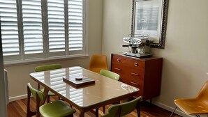 Een eetruimte met een tafel, stoelen, een koffieapparaat en een ingelijst beeld aan de muur.