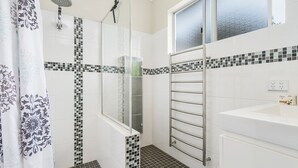Een badkamer met een douche, een douchecabine met glazen wanden, een handdoekrek en een wastafel.