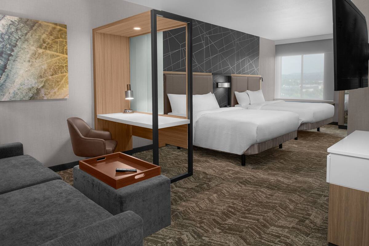 A hotel room with a desk, two beds, a TV, and a view of the city.
