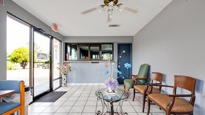 A reception area with a glass-top table, wooden chairs, a blue sofa, and a ceiling fan. - Hotel O Luxury Inn Channelview Baytown I-10 (Channelview)