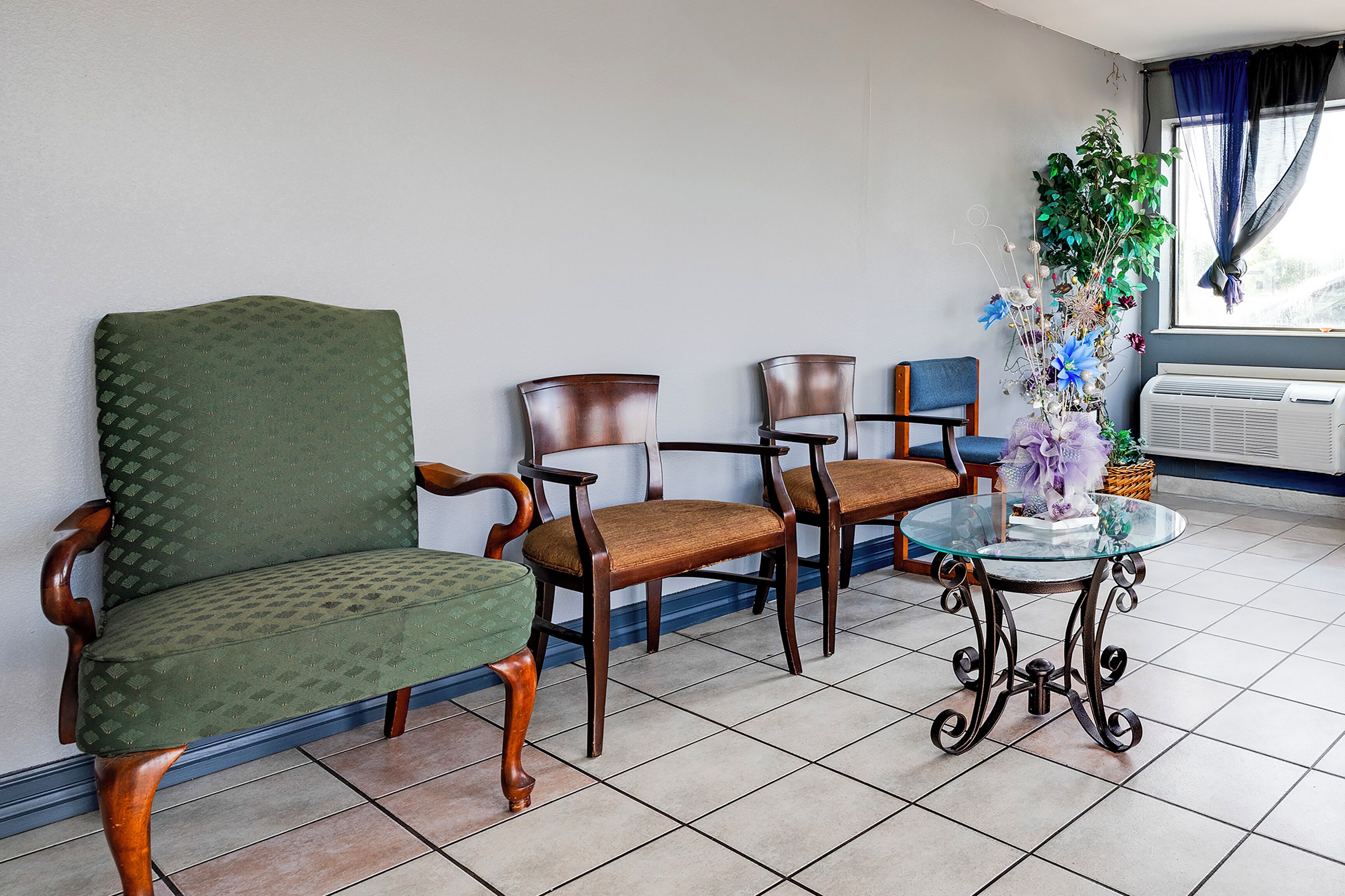 A room with a green upholstered chair, a wooden chair, and a glass table with a decorative centerpiece.
