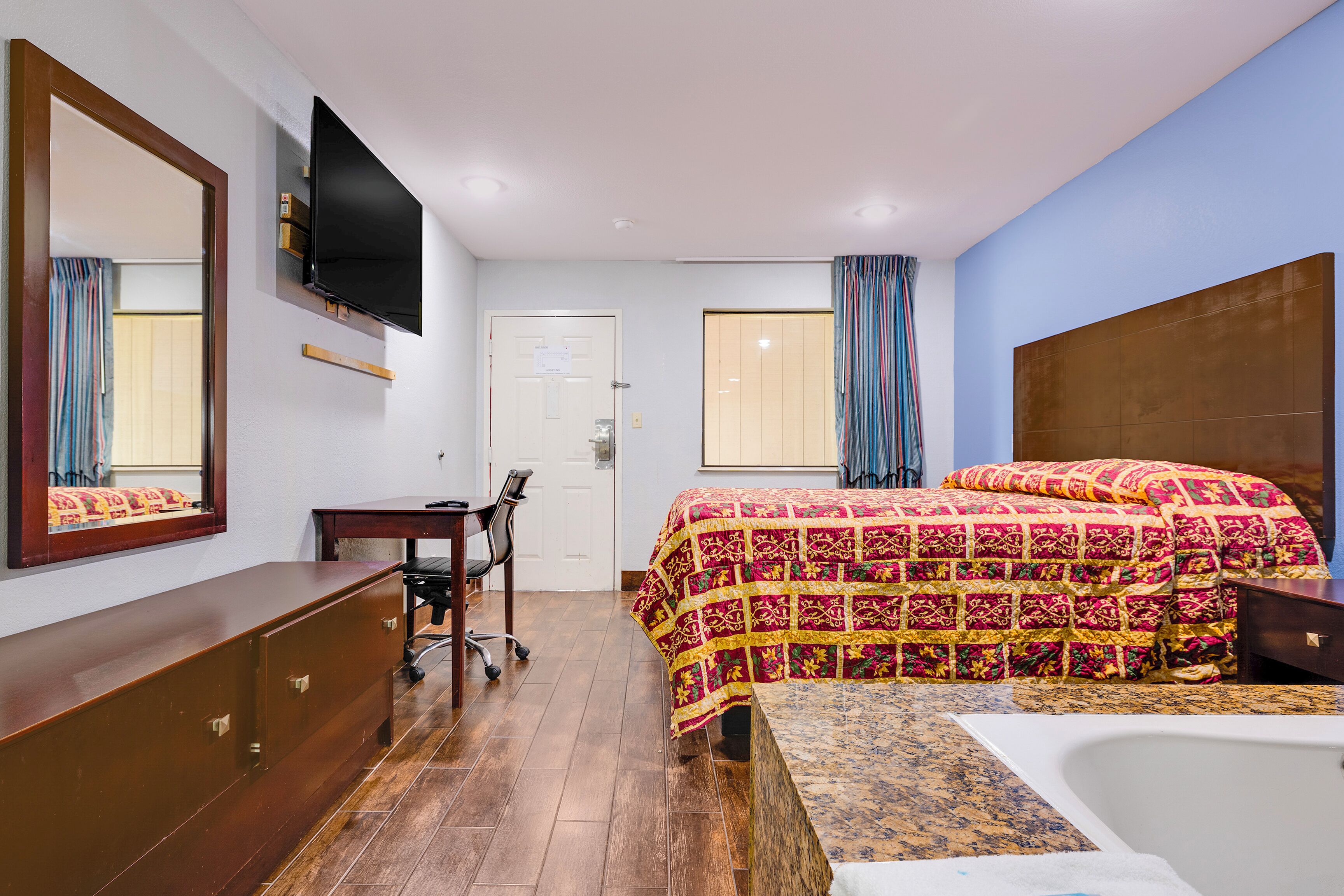 Habitación de hotel con cama, escritorio, silla, televisor montado en la pared y ventana con cortinas.