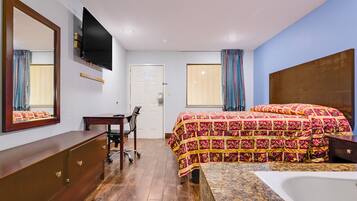 Habitación de hotel con cama, escritorio, silla, televisor montado en la pared y ventana con cortinas.