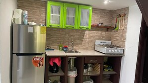 Een kleine keuken met een koelkast van roestvrij staal, een gasfornuis en groene keukenkastjes.