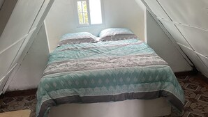 Een kleine zolderkamer met schuine wanden, een bed, een raam en vloerbedekking met een patroon.