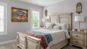 Una camera da letto con un letto grande, un comodino con una lampada, una cassettiera, una finestra con persiane e un quadro appeso al muro.