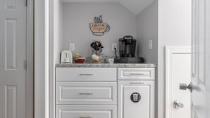 Cucina con mobili bianchi, una macchina per il caffè e un cestino.