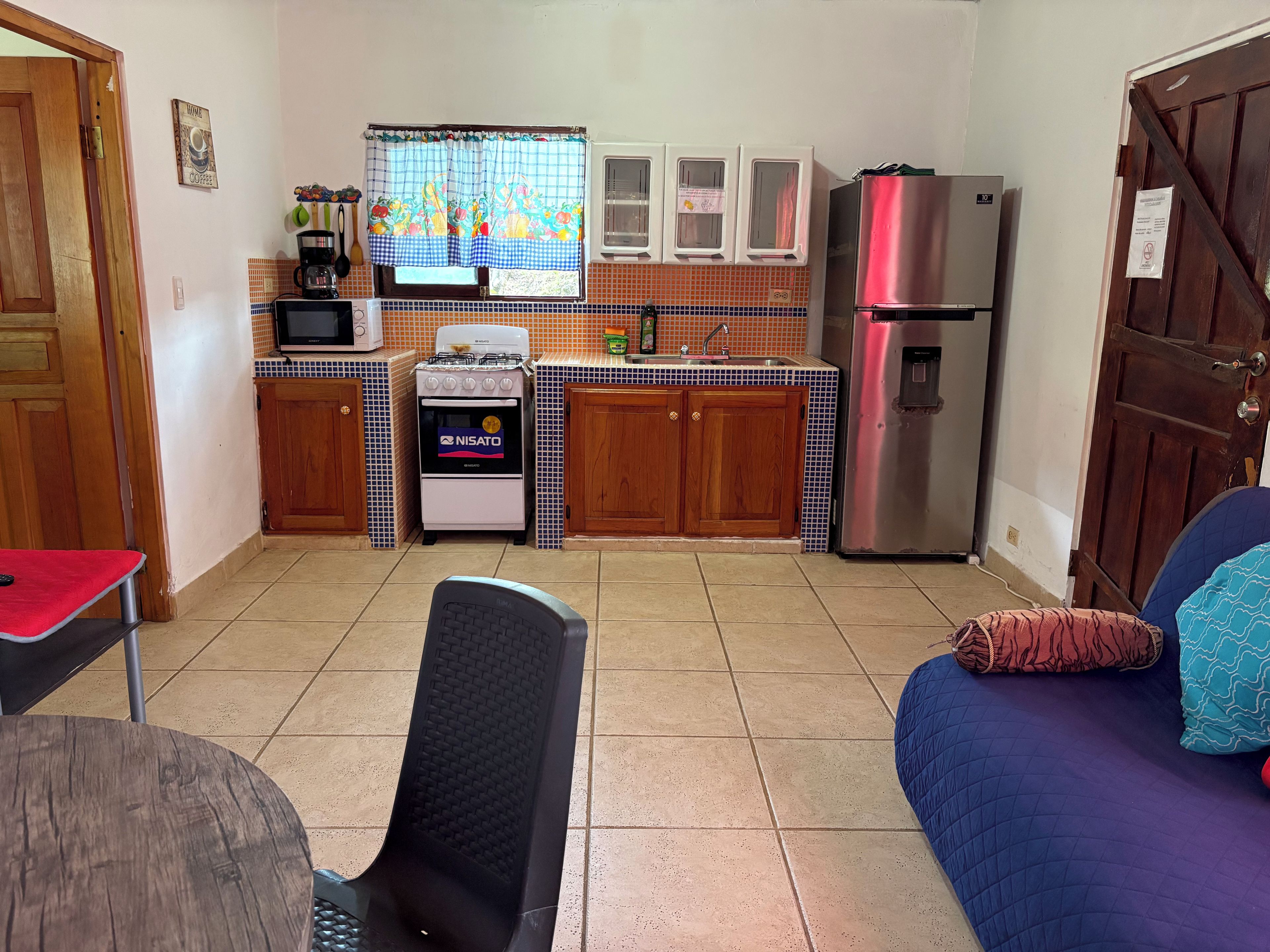 A compact kitchen with a stove, microwave, and refrigerator. There is a dining area with a table and a chair.