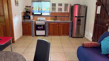 A compact kitchen with a stove, microwave, and refrigerator. There is a dining area with a table and a chair.