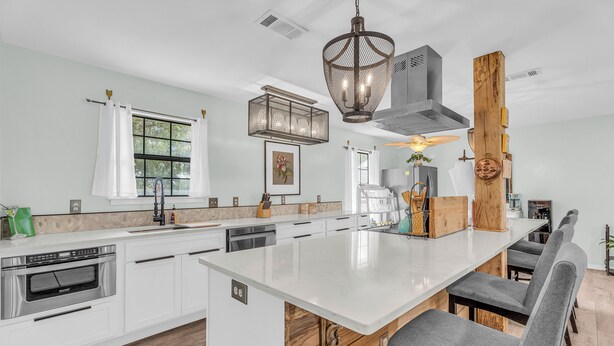 Une cuisine moderne avec des meubles blancs, un îlot central et un luminaire suspendu.