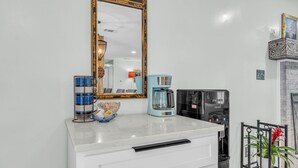 Une cuisine avec un plan de travail blanc, une machine à café, une bouilloire et un appareil électroménager noir.