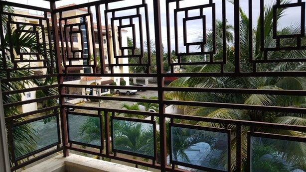 A balcony with a geometric metal railing overlooking a residential area with palm trees and a parked car. - Secure Family-Oriented One of a Kind Condo (Cotui)