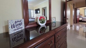 A hotel room with a wooden dresser, a large mirror, a sign with inspirational quotes, and a bed with a TV mounted on the wall. - Secure Family-Oriented One of a Kind Condo (Cotui)