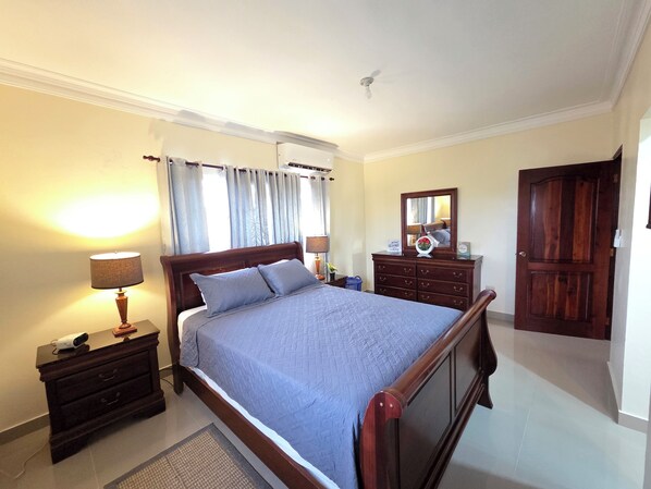 A bedroom with a bed, bedside tables, a dresser, a mirror, a door, and a ceiling fan.