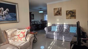 A living room with a sofa, a television, and a dining area in the background. - Secure Family-Oriented One of a Kind Condo (Cotui)