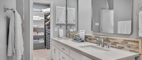 Un baño moderno con tocador blanco, un espejo grande y un vestidor con toallas dobladas con esmero.